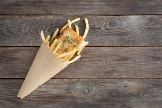 Fish and chips. Overhead view fried fish fillet with french fries wrapped by paper cone, on wooden background.