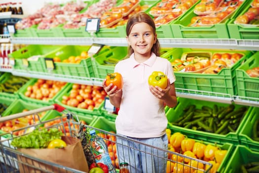 Happy girl looking at camera while choosing peppers in supermarket
