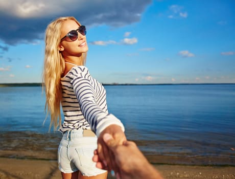 Blond girl holding somebody by hand by the seaside