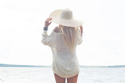 Young woman in hat and white pullover having rest by the sea