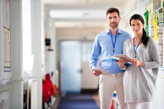 Two teachers standing in a school corridor, they are both dressed smart casual and look serious