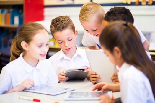 Happy students in classroom using a digital tablet, they are all wearing uniforms.