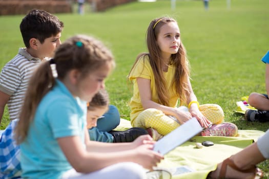Small group of children sitting on the grass having a lesson outdoors. The children look to be listening and enjoying themself.