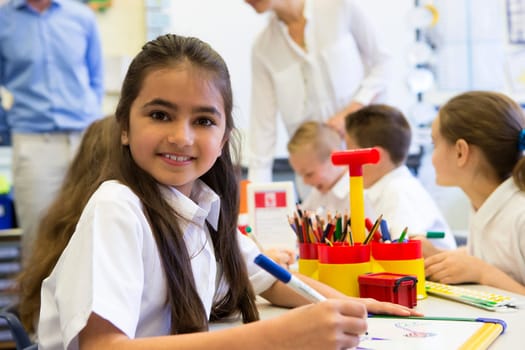 Portrait of a cute young schoolgirl smiling at the camera while sitting at her desk.