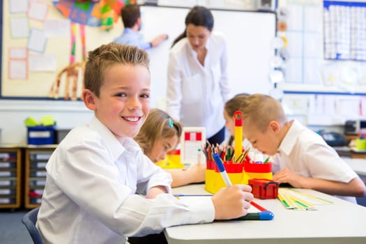 Portrait of a cute young schoolboy smiling at the camera while sitting at his desk.