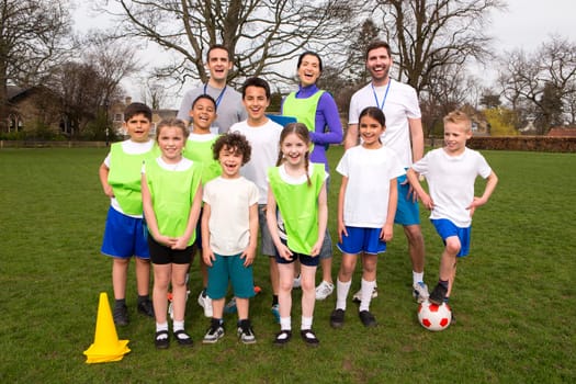 A group portrait of a kids soccer team, behind them are their coaches. They are all smiling and look happy.