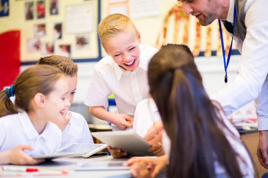 Happy students in classroom using a digital tablet, they are all wearing uniforms.