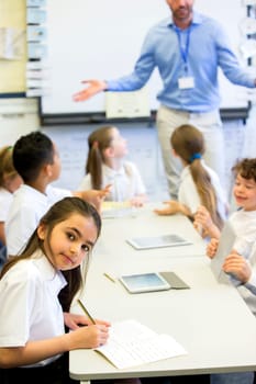 School girl smiles at the camera as she sits at her desk while working.