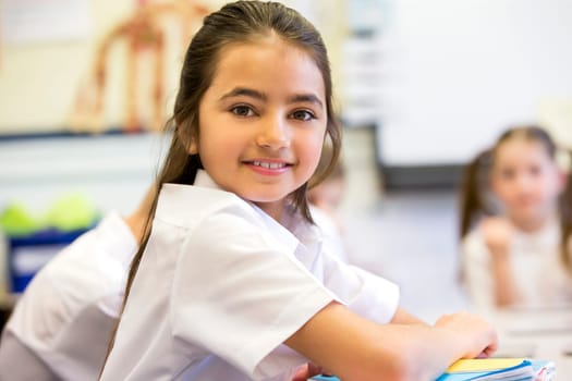 School girl smiles at the camera as she sits at her desk while working.