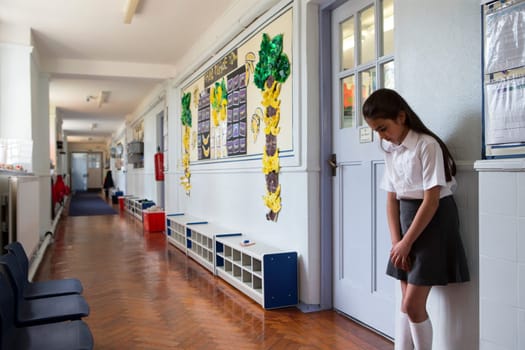 Naughty school girl stands in the corridor after being sent out of class.