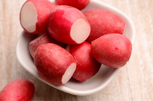 Fresh radishes in a white bowl on a kitchen table