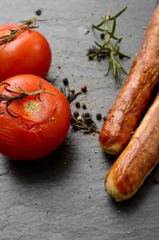 Grilled tomatoes and sausages on a dark slate background