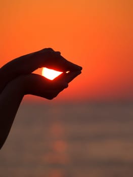 Girl's hands catching the sun at the sunrise near the sea
