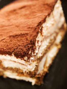 Tiramisu cake in a black plate, close up