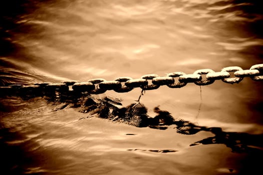 The bizarre and brute ton of an anchor chain protruding from a body of water.