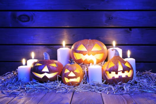four illuminated Halloween pumpkins with candles on straw in front of old weathered wooden boards in blue light
