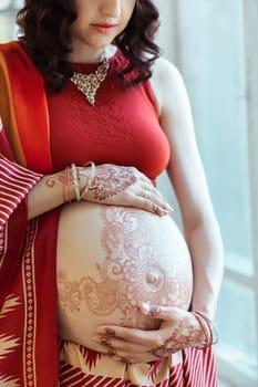 Indian picture on woman hands and pregnant belly with henna tattoo  on white room background