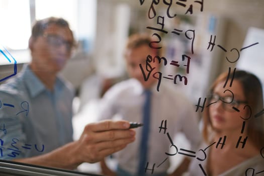 Businessman writing formulae on transparent board