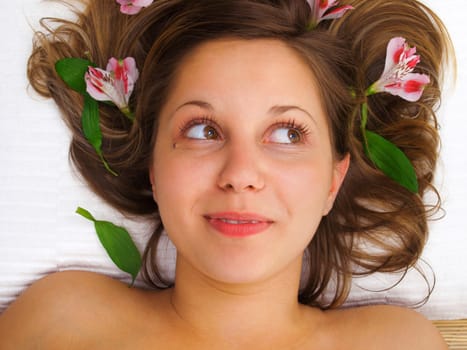 Young woman lying on white background with flowers in her hair waiting in spa studio for massage