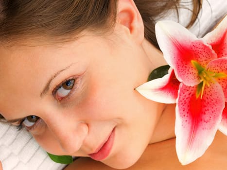 Young woman lying on white background with flowers in her hair waiting in spa studio for massage