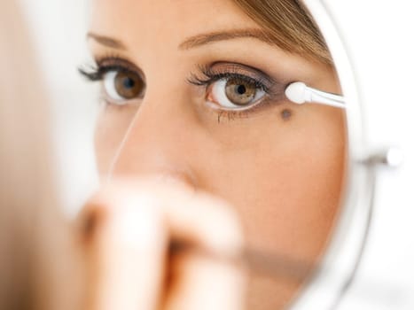 Applying make-up on young woman face, reflection in the mirror