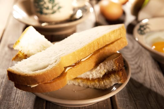 Traditional Chinese Malaysian style breakfast, kaya butter toast and boiled eggs with coffee. Fractal on the cup is generic print. Soft focus setting with dramatic ambient light on dark wooden background.