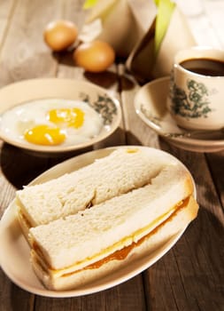 Traditional Malaysian style breakfast, kaya butter toast, nasi lemak and boiled eggs with coffee. Fractal on the cup is generic print. Soft focus setting with dramatic ambient light on dark wooden background.
