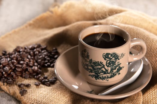 Steaming traditional oriental Chinese kopitiam style dark coffee in vintage mug and saucer with coffee beans. Fractal on the cup is generic print. Soft focus setting with dramatic ambient light on dark wooden background.