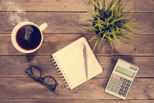 Business analysis concept. Top view workspace with booklet, pen, calculator, glasses and coffee mug. Wooden table background vintage toned.