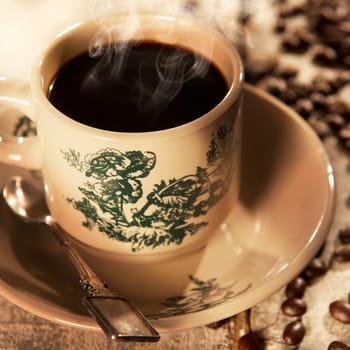 Steaming traditional Hainanese style black coffee in vintage mug and saucer with coffee beans. Fractal on the cup is generic print. Soft focus setting with dramatic ambient light on dark wooden background.