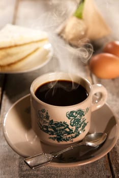 Traditional kopitiam style Malaysian coffee and breakfast with morning sunlight. Fractal on the cup is generic print. Soft focus setting with dramatic ambient light on dark wooden background.