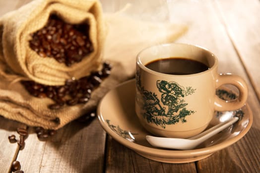 Traditional Chinese style coffee in vintage mug and saucer with coffee beans. Fractal on the cup is generic print. Soft focus setting with dramatic ambient light on dark wooden background.
