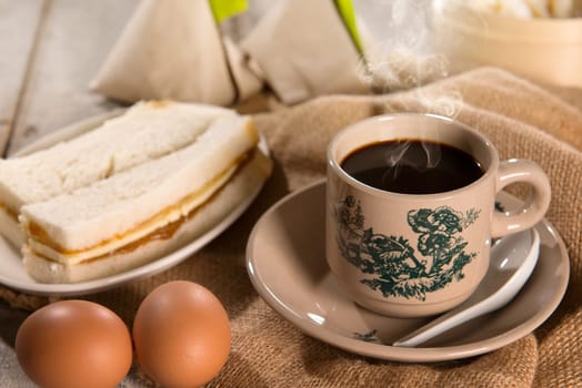 Traditional kopitiam style Malaysian coffee in vintage mug and saucer and breakfast. Fractal on the cup is generic print. Soft focus dramatic ambient light over wood table.