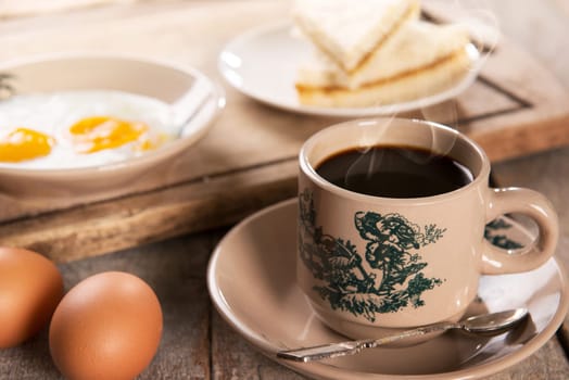 Traditional Singaporean Chinese style coffee in vintage mug and saucer with breakfast. Fractal on the cup is generic print. Soft focus dramatic ambient light over wood table.