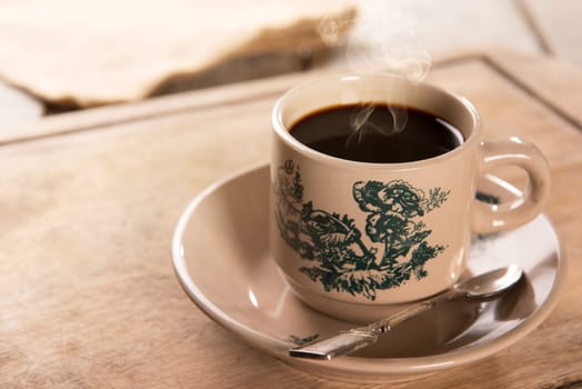 Steaming traditional kopitiam style Malaysian coffee in vintage mug and saucer.  Fractal on the cup is generic print. Soft focus setting with dramatic ambient light on dark wooden background.