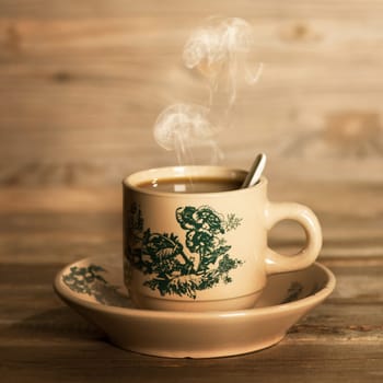 Close up steaming traditional oriental Chinese coffee in vintage mug and saucer.  Fractal on the cup is generic print. Soft focus setting with dramatic ambient light on dark wooden background.