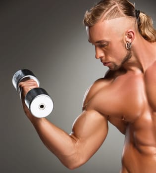 Closeup of a handsome power athletic man bodybuilder doing exercises with dumbbell. Fitness muscular body on dark background.