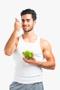 Handsome young man eating a healthy salad, isolated over a gray background