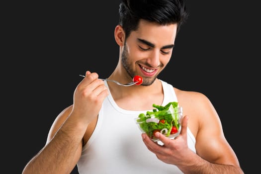 Muscular man eating a healthy salad, isolated over a gray background