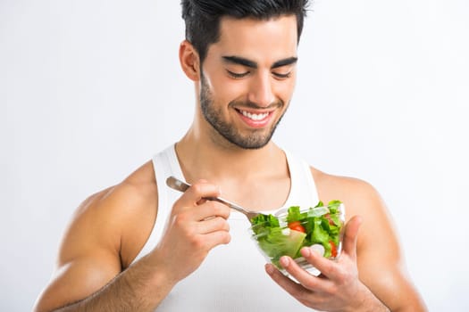 Handsome young man eating a healthy salad, isolated over a gray background