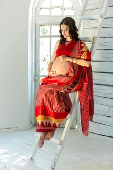 Indian picture on woman mehendi tradition decoration, resistant design by special paint, brown henna. Woman sitting in indian red dress on white wooden staircase background