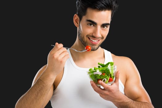 Muscular man eating a healthy salad, isolated over a gray background