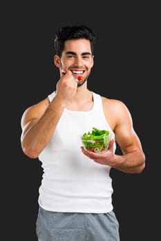 Handsome young man eating a healthy salad, isolated over a gray background