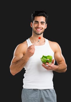 Handsome young man eating a healthy salad, isolated over a gray background