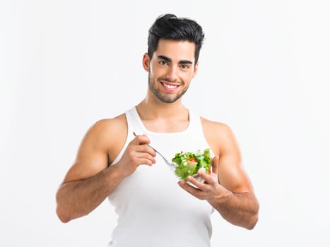 Handsome young man eating a healthy salad, isolated over a gray background