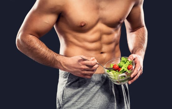 Muscular man eating a healthy salad, isolated over a gray background