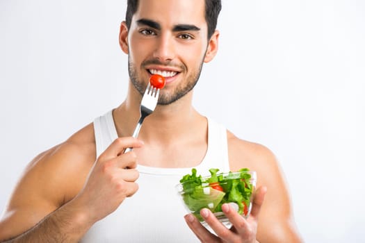 Muscular man eating a healthy salad, isolated over a gray background