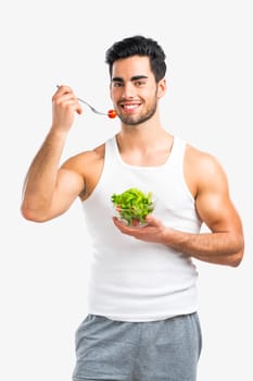 Handsome young man eating a healthy salad, isolated over a gray background