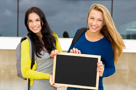 Two beautiful teenage students holding backpacks and smiling