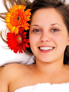 Young woman lying on white background with flowers in her hair waiting in spa studio for massage